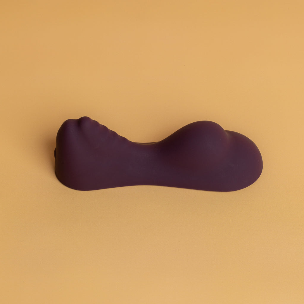 The Ruby Glow by Rocks off sit on hands-free vibrator. The Ruby Glow is purple in colour. The bottom of the vibrator is flat on the bottom to allow for accessibility on different surfaces such as chairs. The front end of the vibrator has a circular bump that then dips into the middle of the vibrator. The back end of the Ruby glow by rocks off vibrator raises from the middle and becomes bumpy until it reaces its peak. It then drops off at the end to allow for the perfect straddle