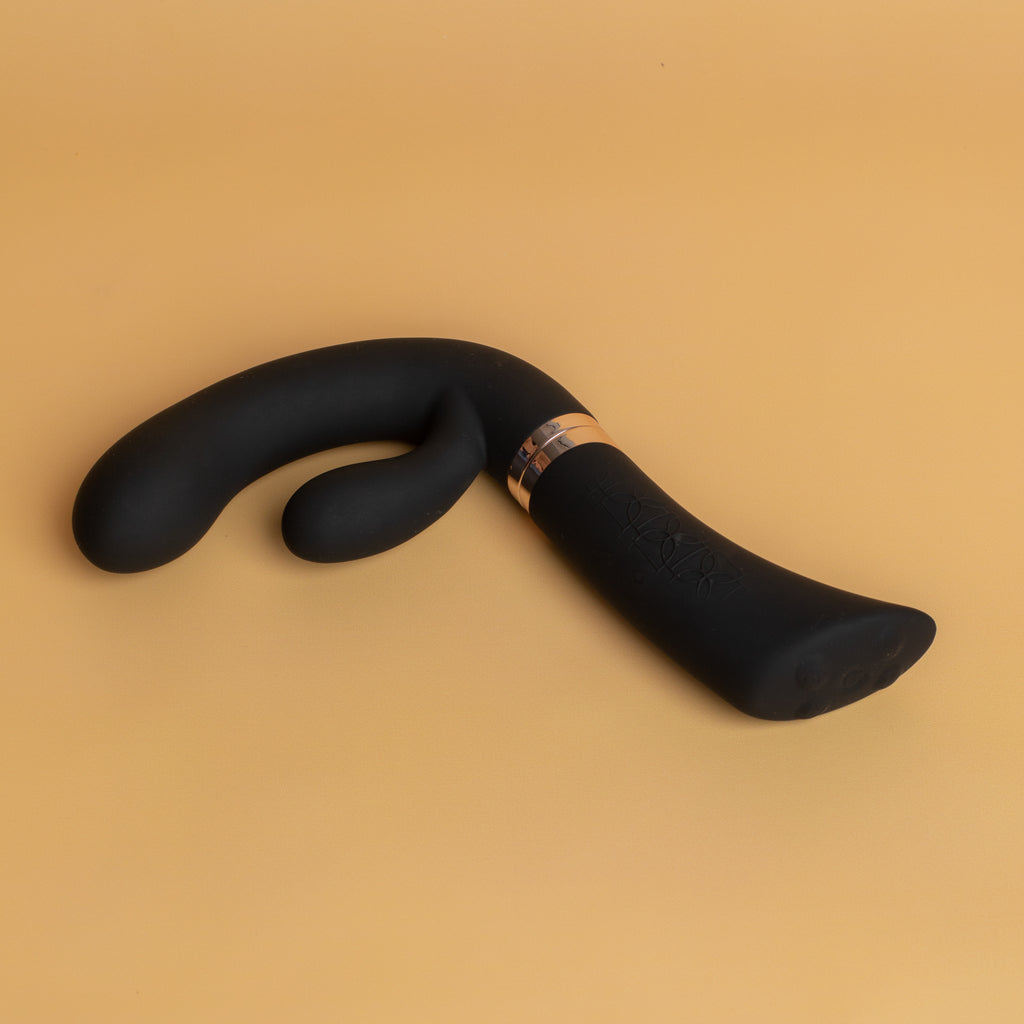 The enigma lying on an orange backdrop. The middle of the enigma (where you can unscrew it and split it into two parts) is gold. The ergonomic handles relieves pressure on joints and improves accessibility to the enigma sex toy, It is stocked at xesproducts.com.au xes products
