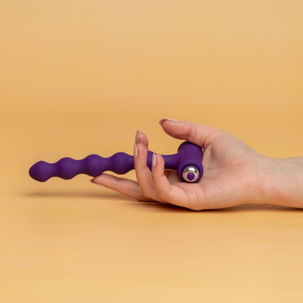 A hand holding the petite sensations pearls purple. There are 5 pearls all the same size. At the end of the petite sensations there is a bullet with a button to turn it on and adjust the settings. 