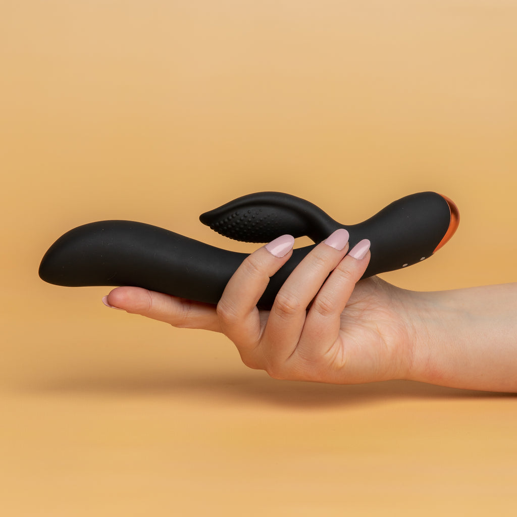 A hand holding the Regala Rabbit by rocks off. The end of the vibrator where they controllers are has a rose gold ABS plating.