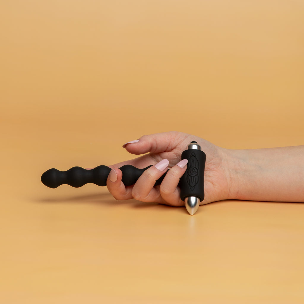 A hand holding the petite sensations pearls black. There are 5 pearls all the same size. At the end of the petite sensations there is a bullet with a button to turn it on and adjust the settings. The bullet can be removed. 