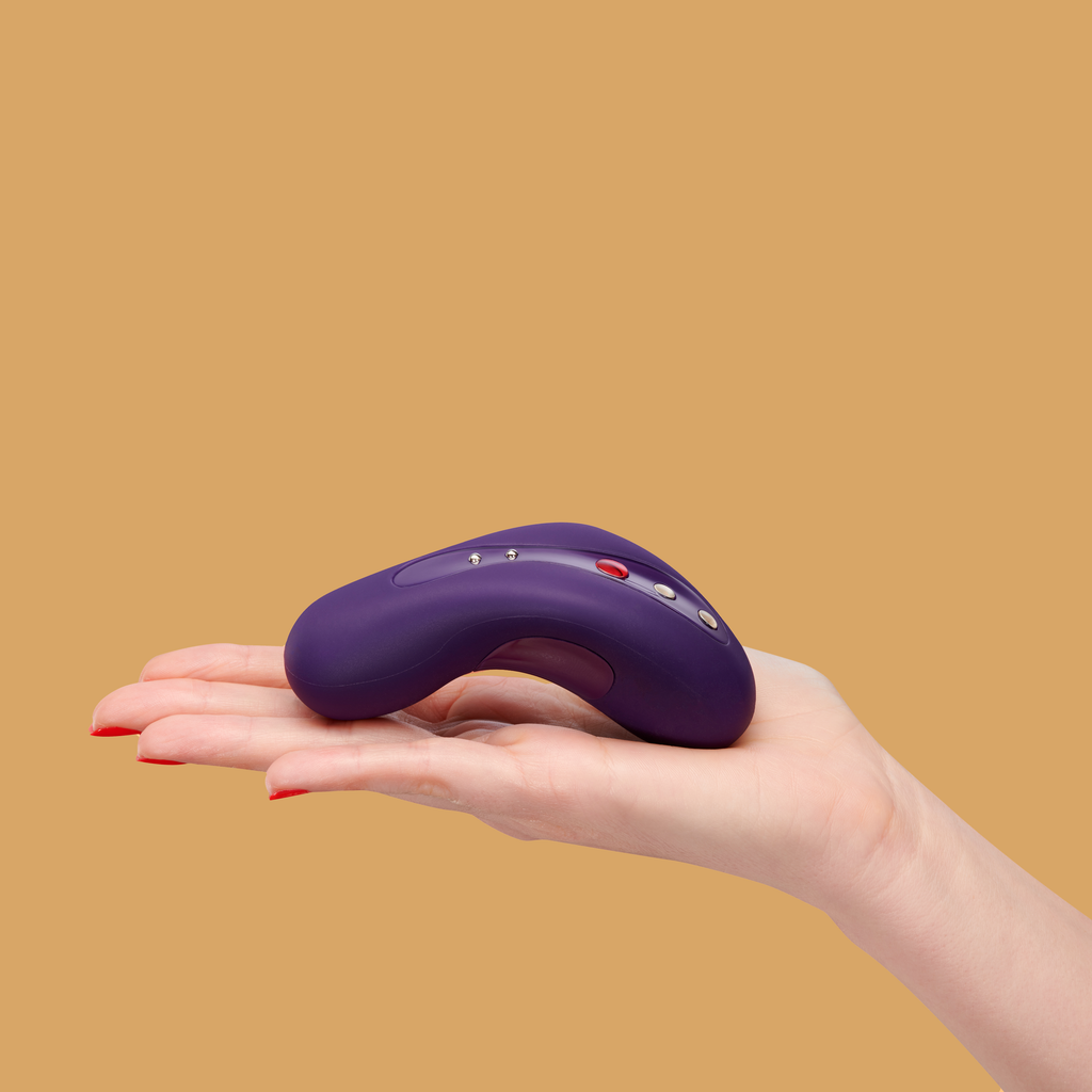 Image of a hand with the Laya 2 by Fun Factory in dark violet resting on top.  That Laya 2 is curved to fit perfectly in the hand with buttons ontop throughout the middle of the toy. 