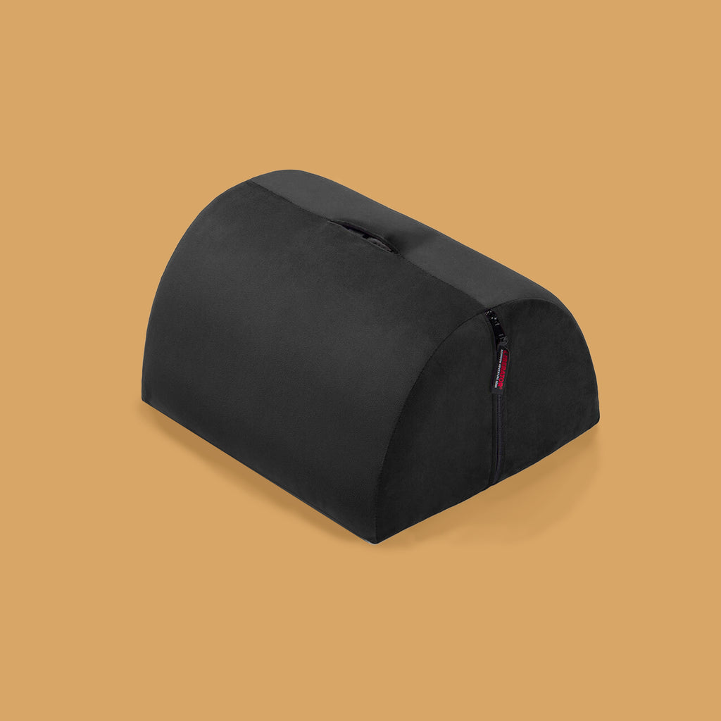 The bon bon positioning pillow. It is black and the shape is half of a cylinder. There is a space in the middle to insert a dildo or other sex toy. The Bon Bon is accessible and disability friendly